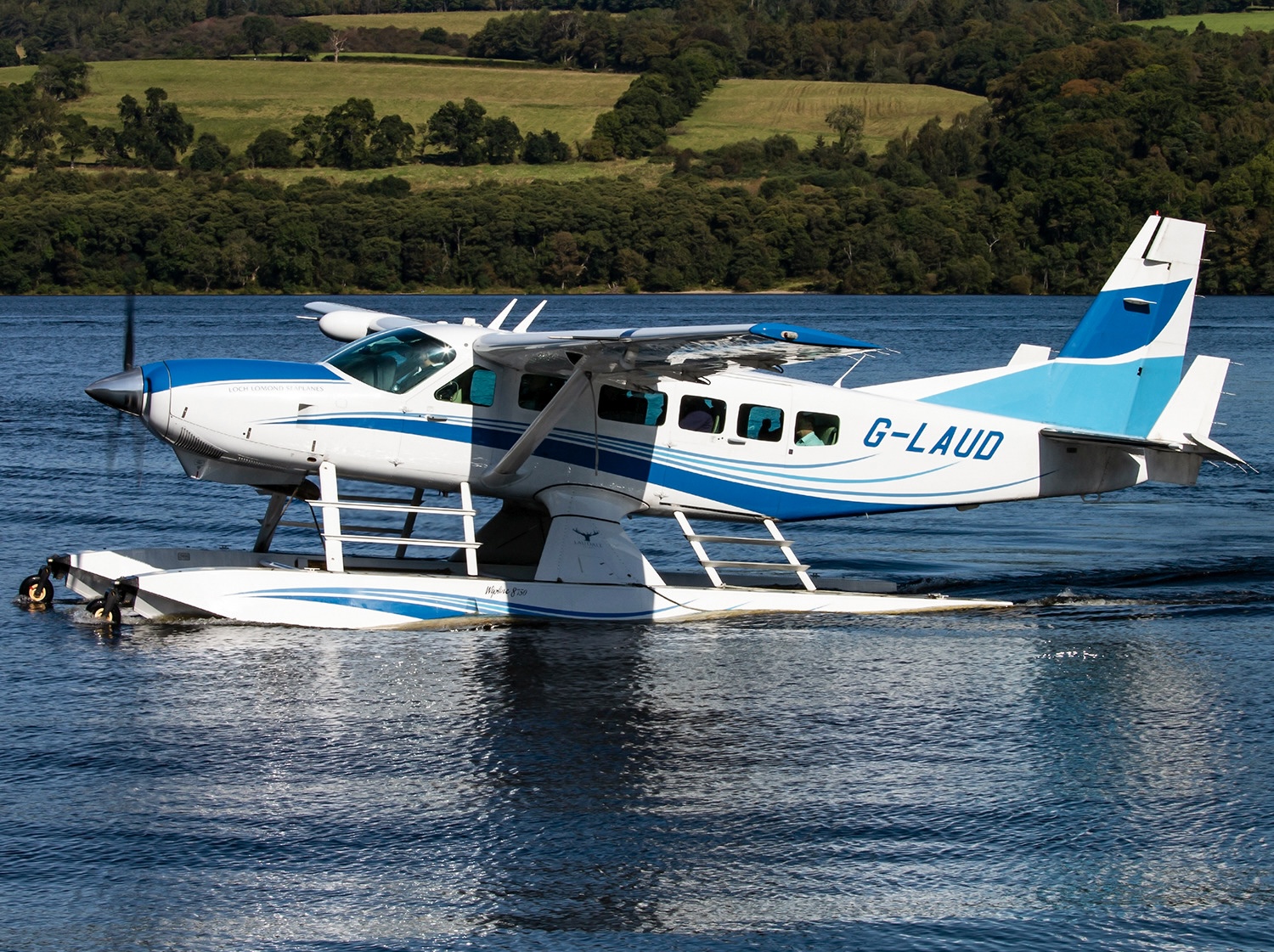 White and blue amphibious Cessna 208 Caravan floatplane, registration G-LAUD, taxiing on a loch